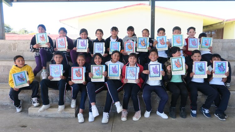 Two rows of about a dozen students each hold up similarly designed butterfly photos they received through the Symbolic Migration Project