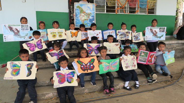 Three rows of children hold up colored butterfly photos sent to them through the Symbolic Migration Project